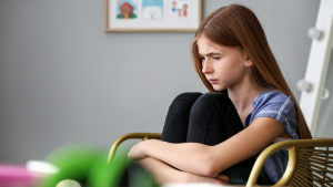 Adolescente autista sentada em uma cadeira, com expressão pensativa e séria, demonstrando sensibilidade e introspecção.