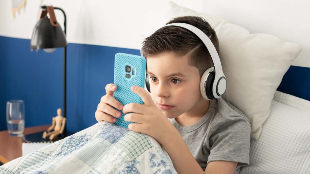 Criança autista usando fones de ouvido e celular, representando desafios da adolescência autista e suporte social.