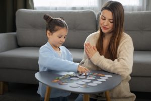Mãe e filha autista interagindo com jogo de cartas para desenvolver comunicação afetiva e reconhecer emoções.