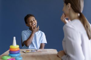 Criança autista em sessão de terapia ocupacional se comunicando por gestos e expressões faciais com a terapeuta.